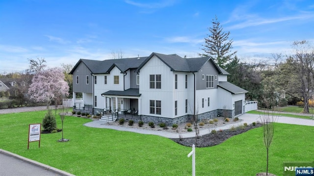 view of front of house with a front lawn, driveway, board and batten siding, covered porch, and a garage