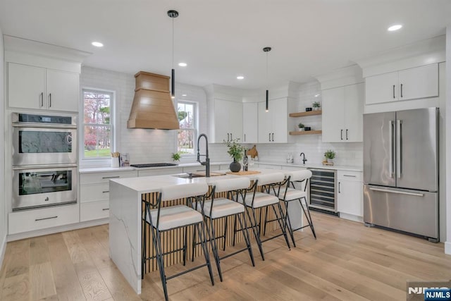 kitchen featuring stainless steel appliances, wine cooler, open shelves, light countertops, and custom range hood