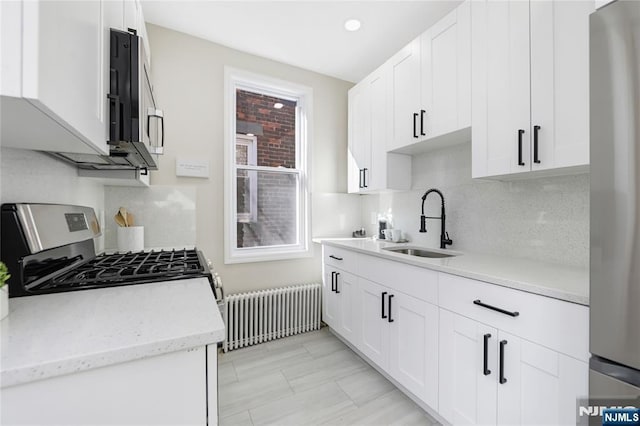 kitchen featuring radiator heating unit, tasteful backsplash, a sink, stainless steel appliances, and white cabinetry