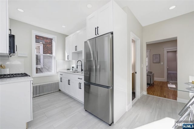 kitchen with a sink, white cabinetry, radiator heating unit, light countertops, and appliances with stainless steel finishes