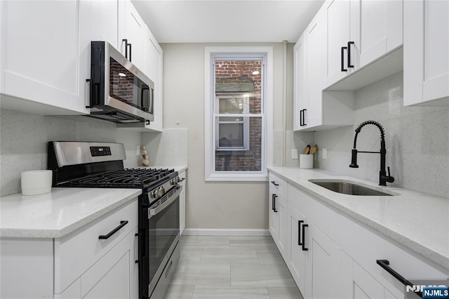 kitchen with tasteful backsplash, a sink, stainless steel appliances, baseboards, and white cabinetry