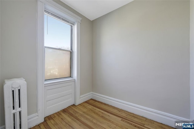 unfurnished room with baseboards, radiator heating unit, and light wood-style floors
