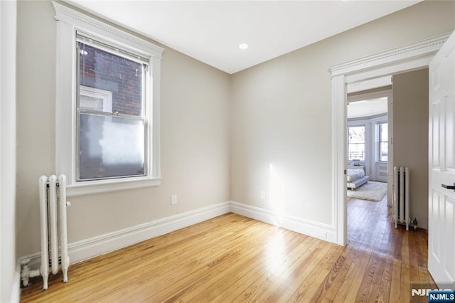 empty room featuring hardwood / wood-style flooring, radiator, and baseboards