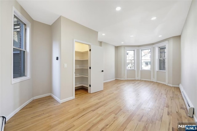 unfurnished bedroom featuring baseboards, a spacious closet, light wood finished floors, and baseboard heating