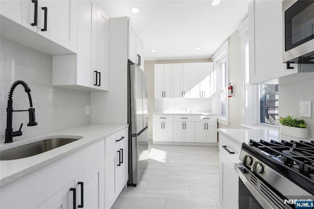 kitchen with stainless steel appliances, a sink, recessed lighting, backsplash, and white cabinetry