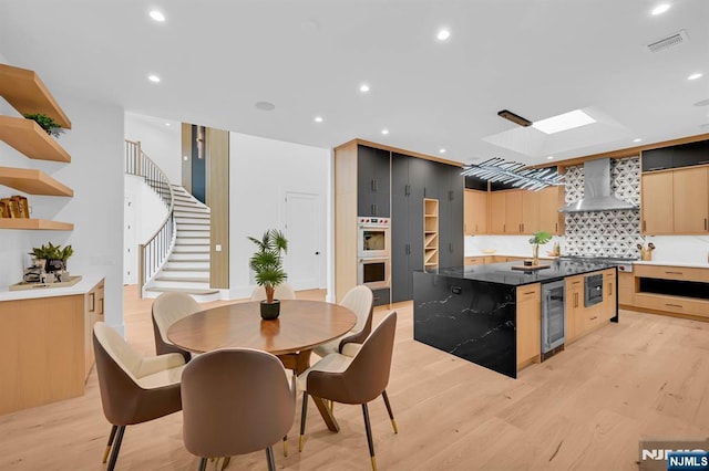 kitchen with wall chimney range hood, beverage cooler, visible vents, and light wood-style flooring