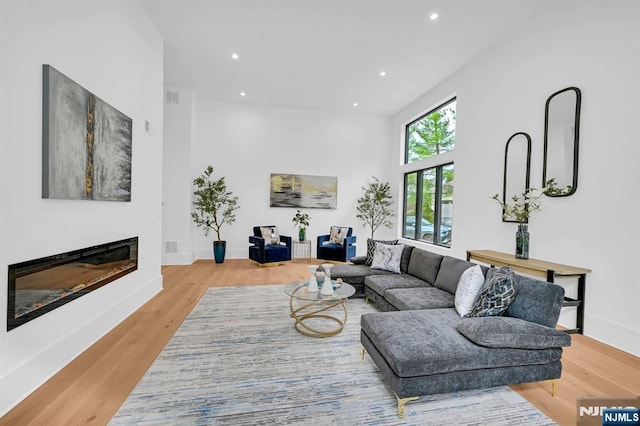 living area with recessed lighting, a glass covered fireplace, wood finished floors, and baseboards