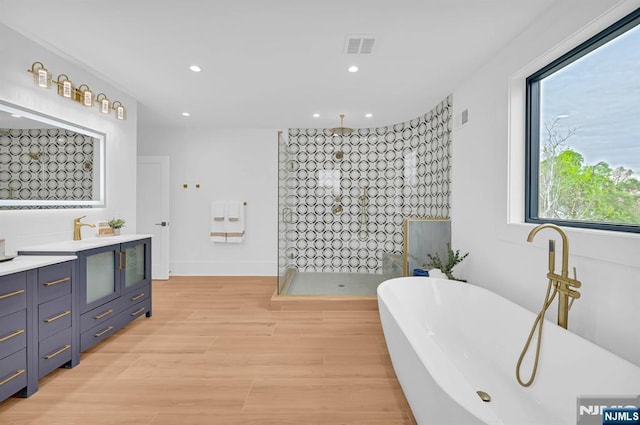 full bathroom featuring a freestanding bath, wood finished floors, visible vents, vanity, and a walk in shower