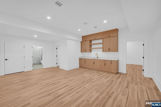 kitchen featuring a sink, baseboards, visible vents, light wood-style floors, and light countertops