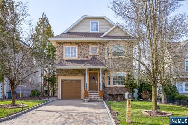 view of front of property featuring decorative driveway, stone siding, a shingled roof, an attached garage, and a front yard
