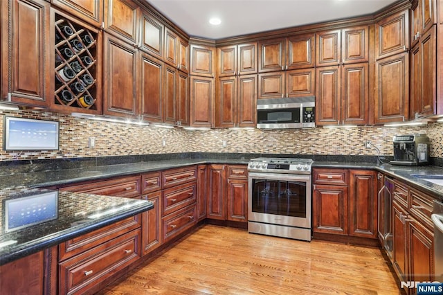 kitchen with light wood-type flooring, stainless steel appliances, backsplash, and dark stone counters