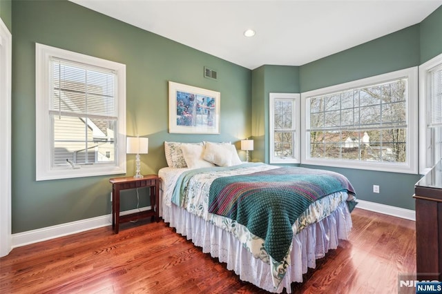bedroom featuring baseboards, wood finished floors, visible vents, and multiple windows