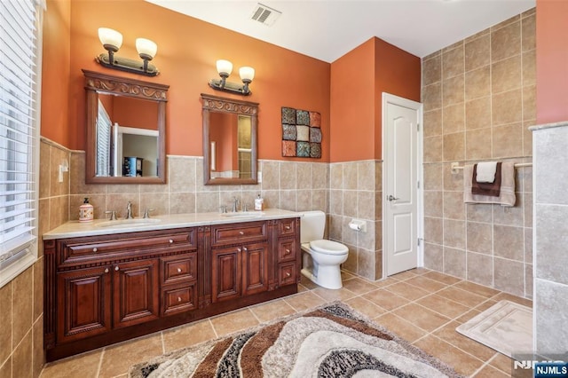 full bath featuring a sink, tile walls, double vanity, toilet, and visible vents