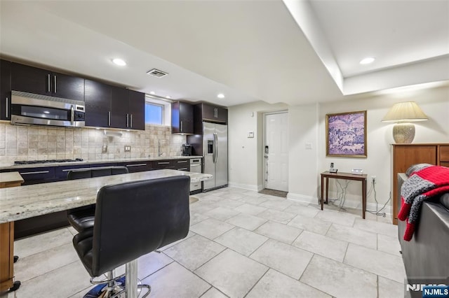 kitchen featuring stainless steel appliances, visible vents, light stone countertops, baseboards, and tasteful backsplash