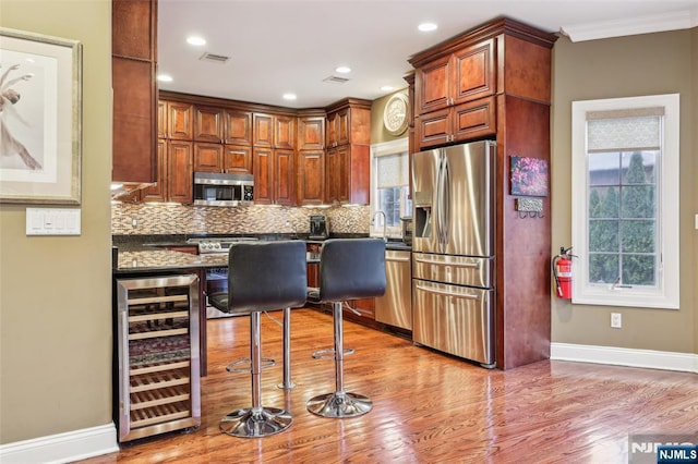 kitchen featuring beverage cooler, stainless steel appliances, visible vents, light wood-type flooring, and tasteful backsplash
