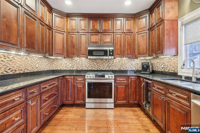 kitchen with beverage cooler, stainless steel appliances, a sink, light wood-type flooring, and tasteful backsplash