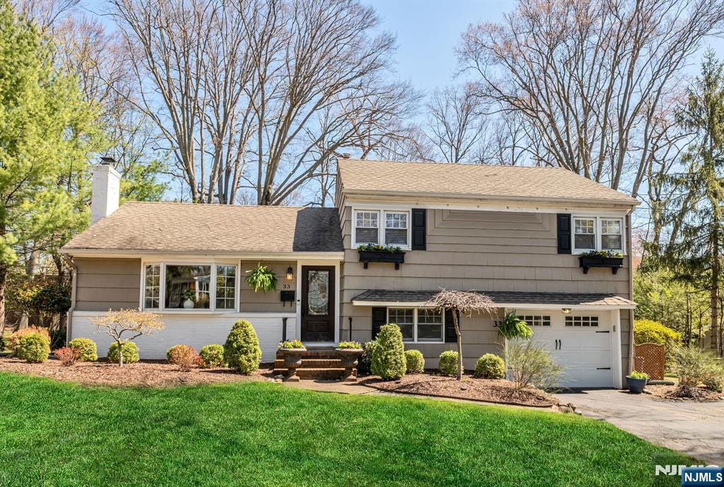 tri-level home with an attached garage, a front lawn, a chimney, and concrete driveway
