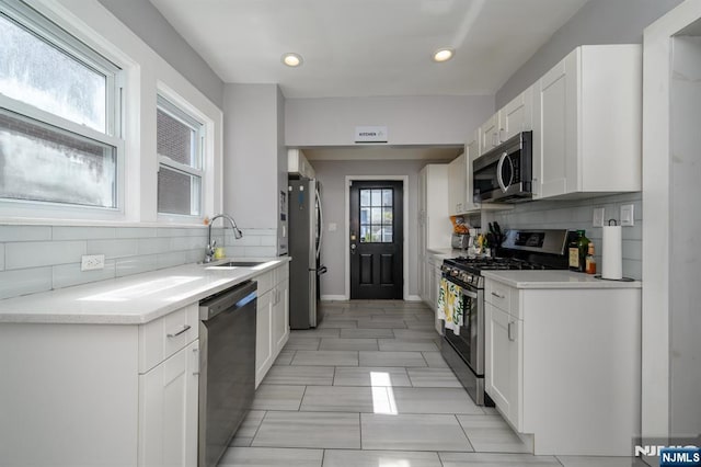 kitchen featuring appliances with stainless steel finishes, white cabinetry, tasteful backsplash, and a sink