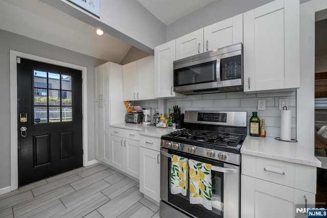 kitchen with decorative backsplash, white cabinetry, baseboards, appliances with stainless steel finishes, and lofted ceiling