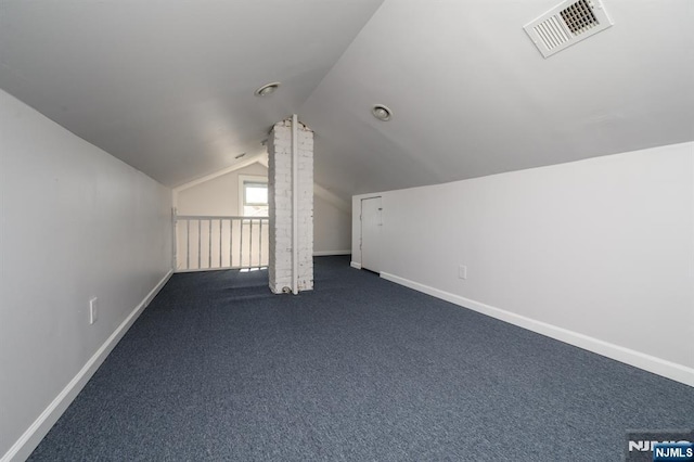 additional living space with baseboards, visible vents, dark colored carpet, and lofted ceiling