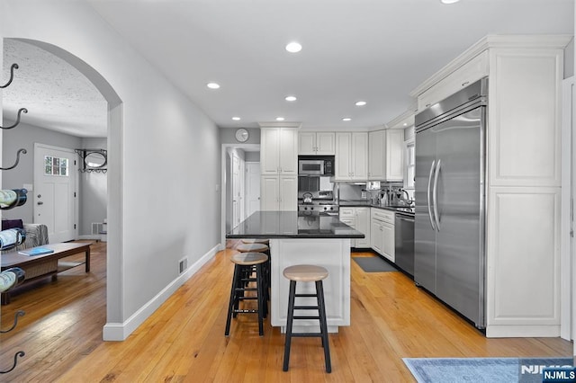 kitchen featuring baseboards, white cabinets, stainless steel appliances, and arched walkways