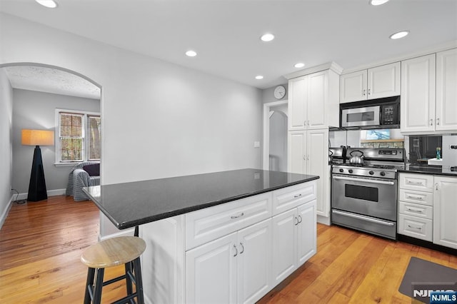 kitchen featuring dark countertops, light wood-type flooring, gas stove, and arched walkways