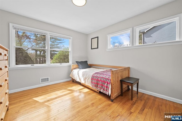 bedroom featuring visible vents, baseboards, light wood finished floors, and multiple windows