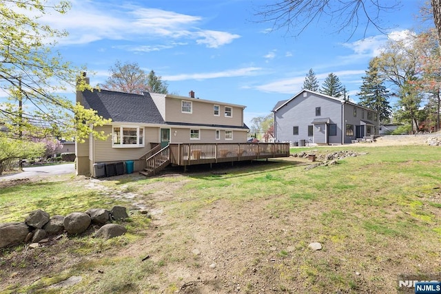 back of property featuring a chimney, a deck, and a yard
