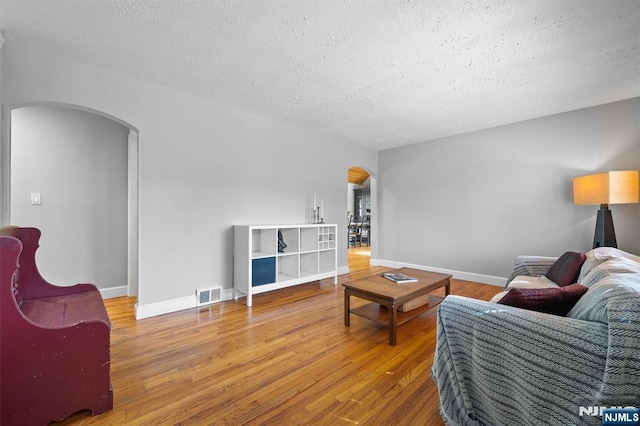 living area with visible vents, arched walkways, a textured ceiling, and wood finished floors