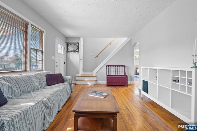 living room with a textured ceiling, hardwood / wood-style flooring, arched walkways, and stairs