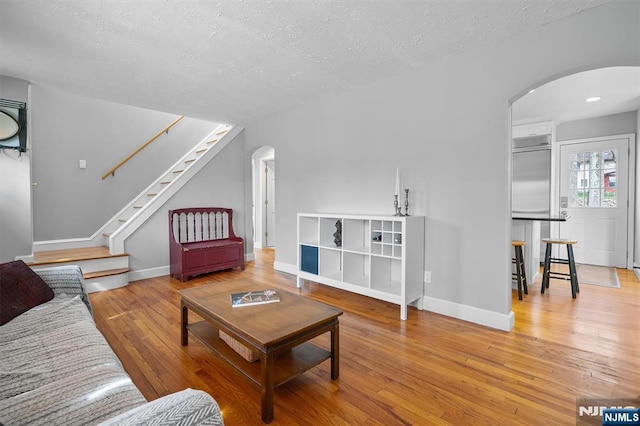 living area with arched walkways, stairs, a textured ceiling, and light wood-style floors