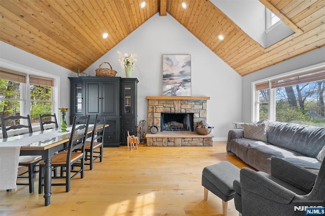 living room with a skylight, light wood-style flooring, wood ceiling, a stone fireplace, and high vaulted ceiling