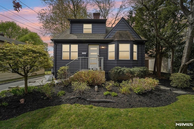bungalow-style home featuring a lawn, a chimney, and roof with shingles