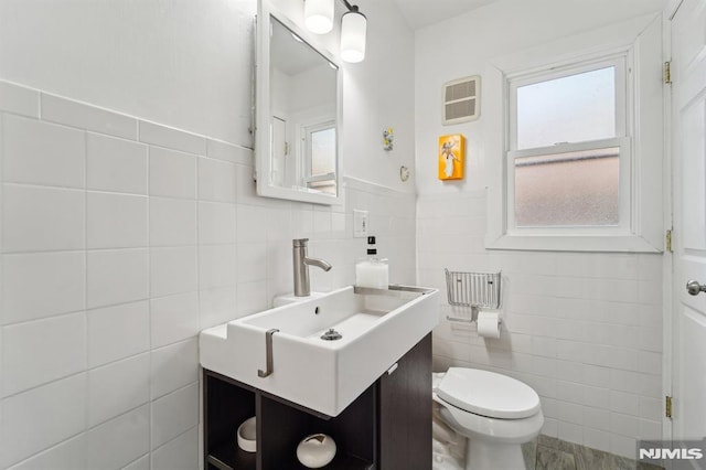 half bath with toilet, tile walls, visible vents, and vanity