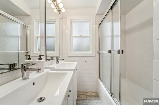 bathroom featuring enclosed tub / shower combo, double vanity, tile walls, and a sink
