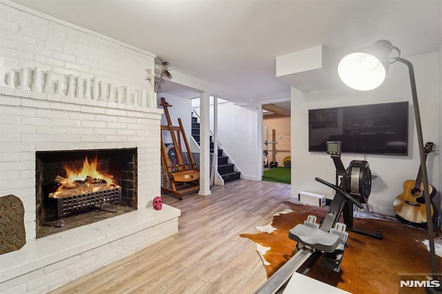 living area featuring stairs, a brick fireplace, and wood finished floors