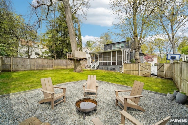 view of yard featuring a fenced backyard, a gate, a sunroom, and an outdoor fire pit