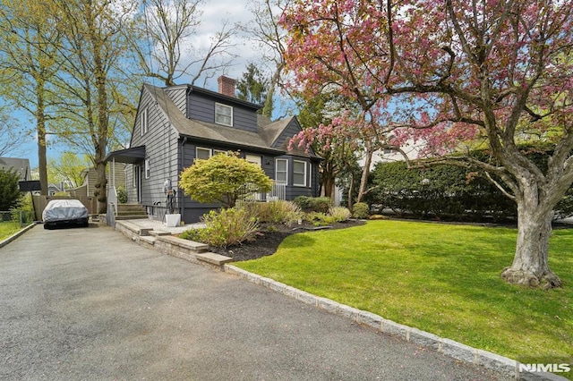 view of side of home with a chimney, a yard, and aphalt driveway
