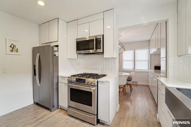 kitchen featuring tasteful backsplash, modern cabinets, light countertops, stainless steel appliances, and white cabinetry