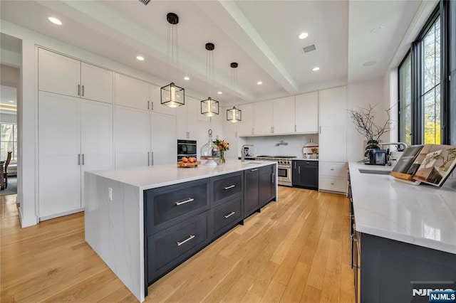 kitchen featuring stainless steel range, a large island with sink, light wood finished floors, dark cabinetry, and white cabinetry