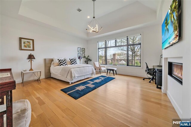 bedroom featuring a raised ceiling, light wood-type flooring, a notable chandelier, and baseboards