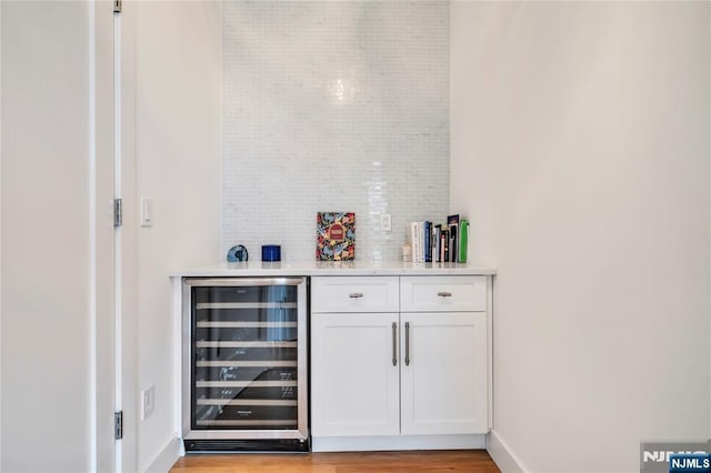 bar with decorative backsplash, beverage cooler, baseboards, a dry bar, and light wood-type flooring