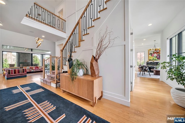 stairway featuring recessed lighting, a high ceiling, a notable chandelier, baseboards, and wood finished floors