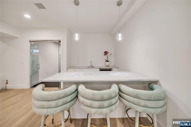 kitchen featuring light wood-style flooring, a kitchen bar, light stone countertops, a peninsula, and hanging light fixtures