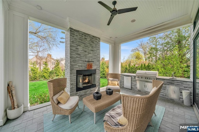 sunroom featuring area for grilling, ceiling fan, and a warm lit fireplace