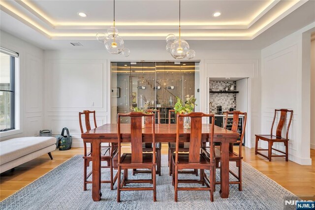 dining room with a decorative wall, wood finished floors, recessed lighting, and a tray ceiling