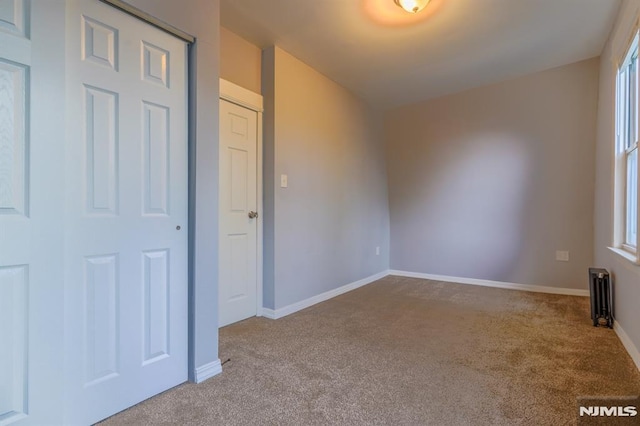 unfurnished bedroom with radiator heating unit, baseboards, and carpet