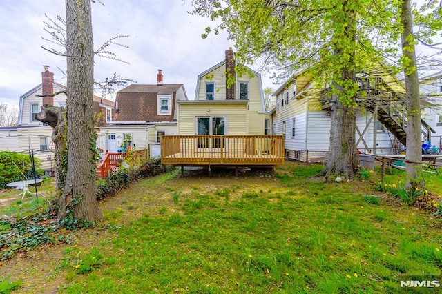 rear view of property featuring a gambrel roof, a chimney, fence, a yard, and a deck