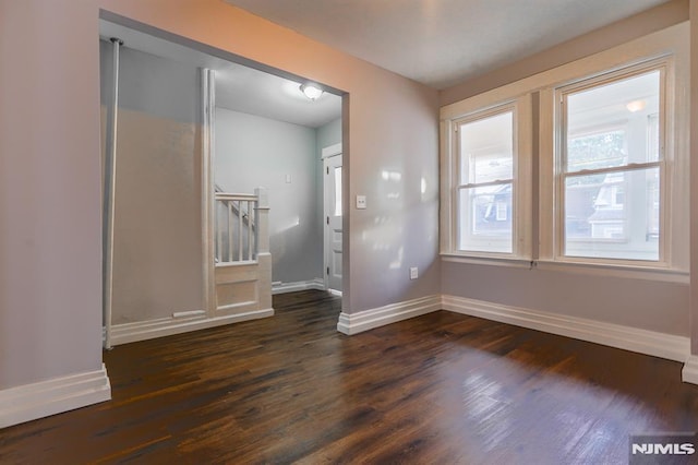 empty room featuring stairway, baseboards, and dark wood-type flooring