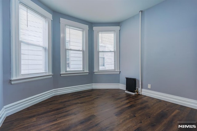 empty room featuring baseboards, radiator heating unit, and dark wood-style floors